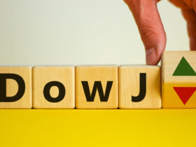 Male hand flips a wooden cube and changes the inscription 'DowJ up' to 'DowJ down'. Beautiful yellow table, white background. Business, interest rate, stocks, financial, ranking, mortgage rates and concept.