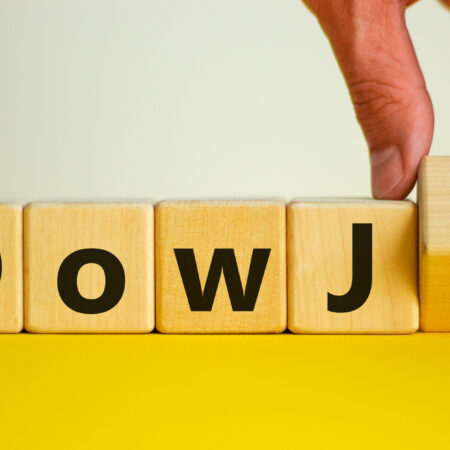 Male hand flips a wooden cube and changes the inscription 'DowJ up' to 'DowJ down'. Beautiful yellow table, white background. Business, interest rate, stocks, financial, ranking, mortgage rates and concept.