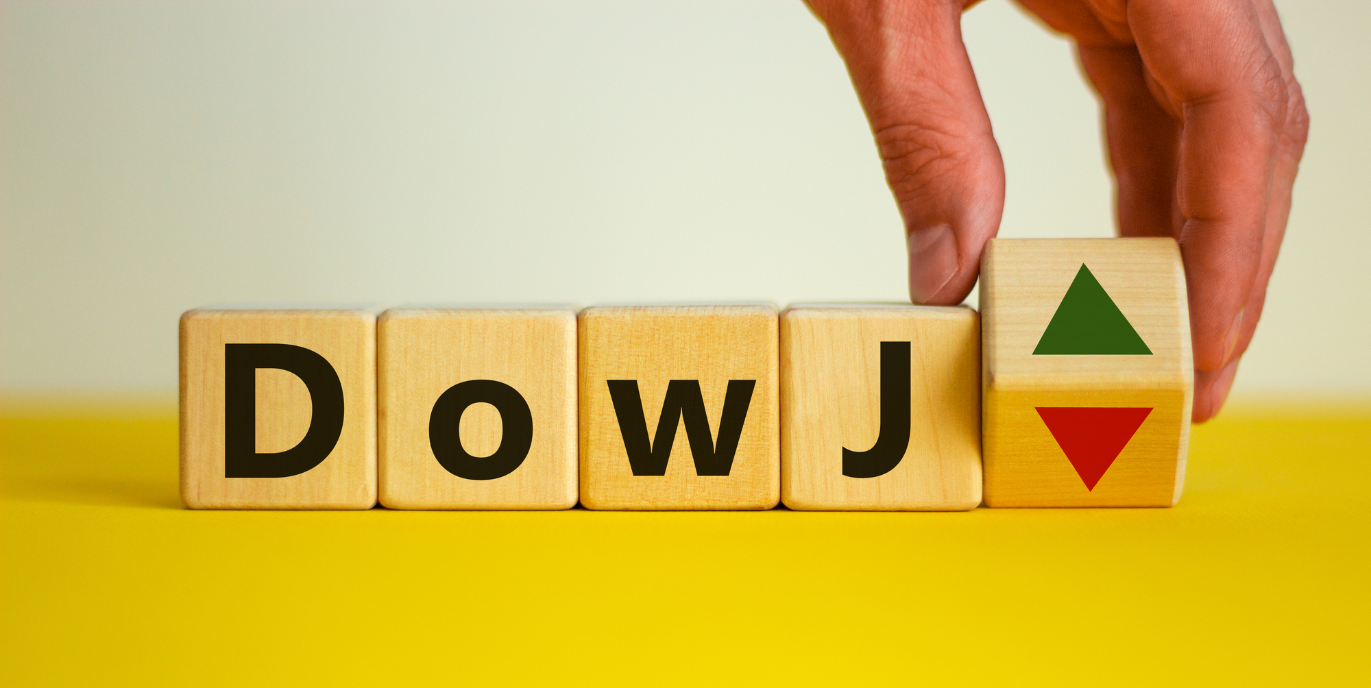 Male hand flips a wooden cube and changes the inscription 'DowJ up' to 'DowJ down'. Beautiful yellow table, white background. Business, interest rate, stocks, financial, ranking, mortgage rates and concept.